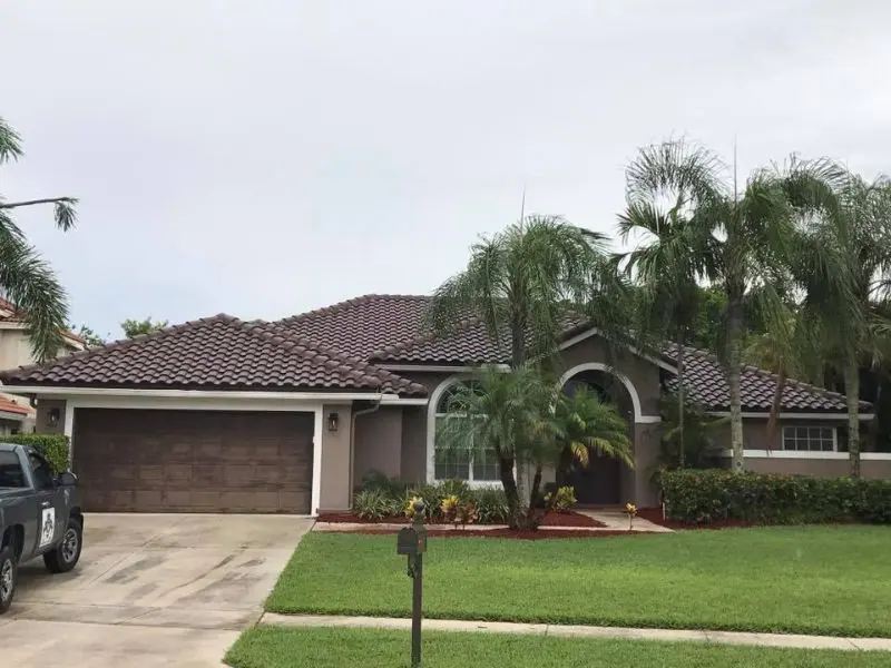 Stucco home with arched windows and a dark concrete tile roof framed by palms