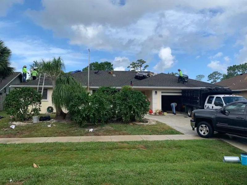 Roofing crew in safety green laying new shingles on a Palm Beach County home