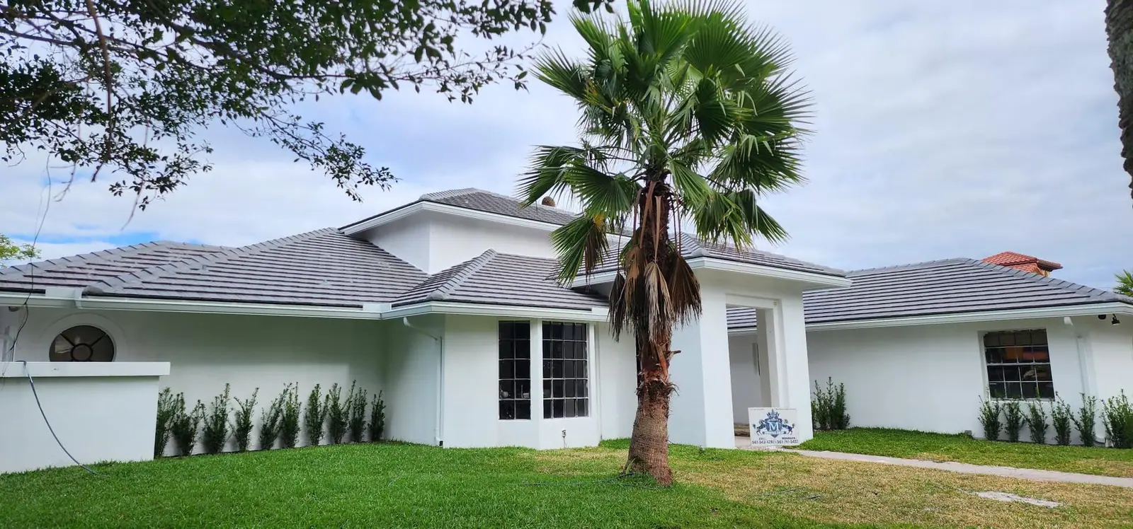 White Palm Beach County home with a new flat concrete tile roof, a palm tree and the Mendieta Roofing yard sign