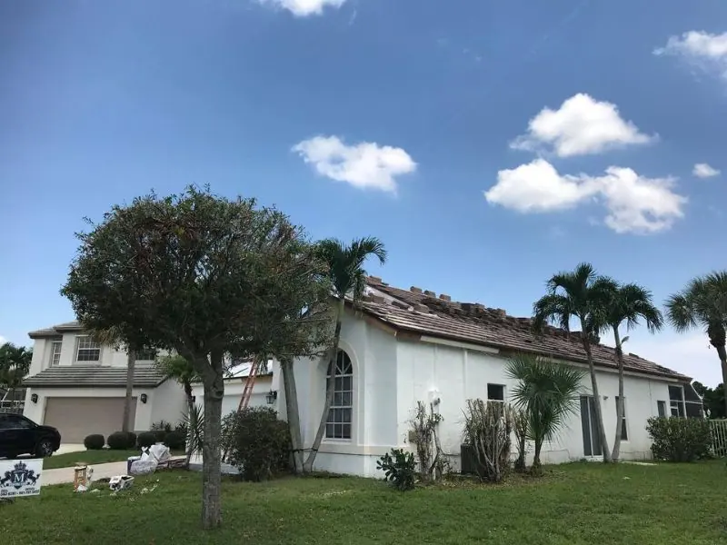White two-story home mid re-roof with new tile stacked along the roof line
