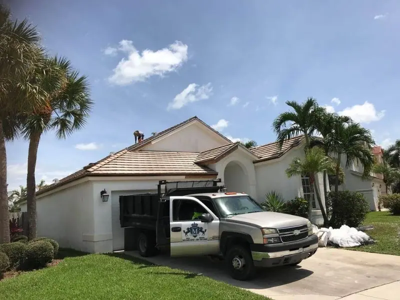 Mendieta Roofing crew truck in the driveway of a white tile roof job, materials bagged on the lawn