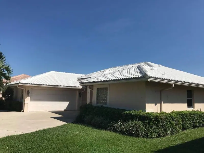 Single-story home with a white flat concrete tile roof and a trimmed hedge